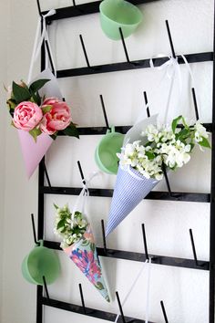 three ice cream cones are hanging on a wall with flowers in them and one has an umbrella