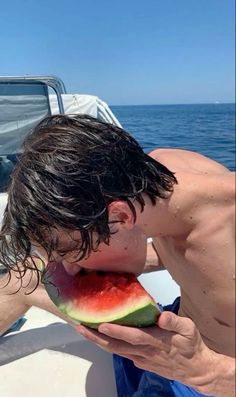 a man eating a piece of watermelon on a boat with the ocean in the background