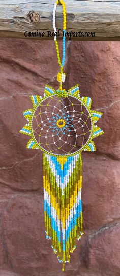 a colorful beaded dream catcher hanging on a wooden pole next to a stone wall