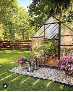 a small greenhouse in the middle of a yard with potted plants and flowers inside