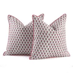 two pillows sitting side by side on top of a white surface with red piping