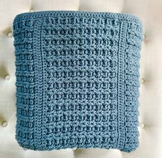 a blue crocheted pillow sitting on top of a white couch