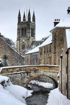 snow covers the ground and buildings in front of a river with a bridge over it