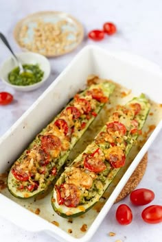 an image of stuffed zucchini with tomatoes and pesto on the side in a baking dish