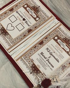 two red and gold wedding cards on top of each other next to a white feather