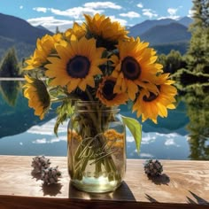 sunflowers are in a mason jar on a wooden table near water and mountains