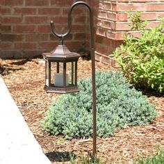 a lamp post with a candle on it in front of a brick wall and shrubbery