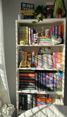 a bookshelf filled with lots of books next to a white bed in a room