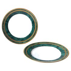 two green and gold plates sitting next to each other on a white surface with an oval design