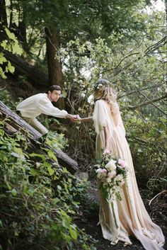 a bride and groom are holding hands in the woods with greenery on either side