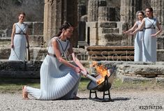 two women in white dresses are cooking over an open fire