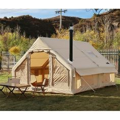 a tent set up in the grass with two chairs and a table next to it