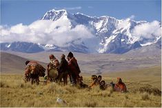 some people are sitting in the grass with mountains in the backgrouds and snow capped peaks behind them