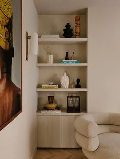 a white chair sitting in front of a book shelf filled with books and vases