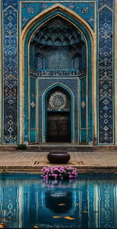 the entrance to an ornate building with blue tiles and flowers in the water below it