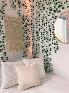 a white bed topped with pillows next to a wall covered in vines and string lights