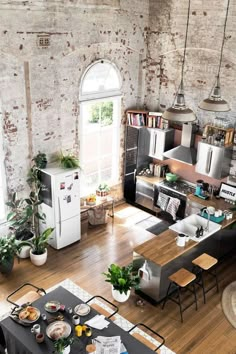 an aerial view of a kitchen and living room with exposed brick walls, hardwood floors, potted plants, and appliances