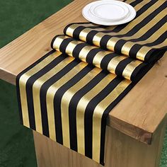 black and gold striped table runner with white plate on wooden bench in front of green grass