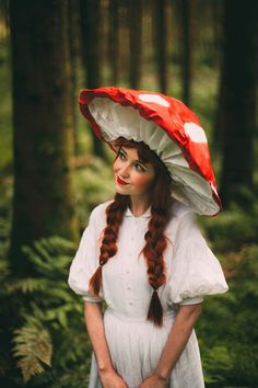 a woman with long hair wearing a red and white mushroom hat in the middle of a forest