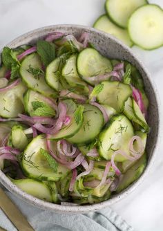 a bowl filled with cucumbers and onions on top of a white table cloth