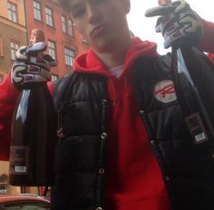 a young man holding two bottles of wine in his hands while standing next to a car