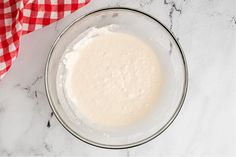 a glass bowl filled with batter sitting on top of a counter next to a red and white checkered napkin