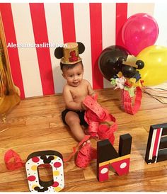 a baby is sitting on the floor next to some letters and balloons in front of him