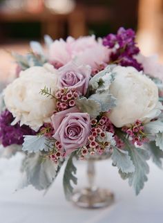 a vase filled with lots of flowers on top of a white table cloth covered table