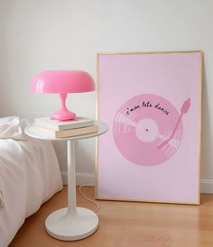 a pink lamp next to a white table with a record on it and a pink poster