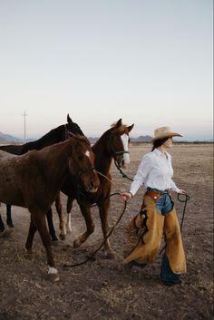 a man leading three horses across a dirt field