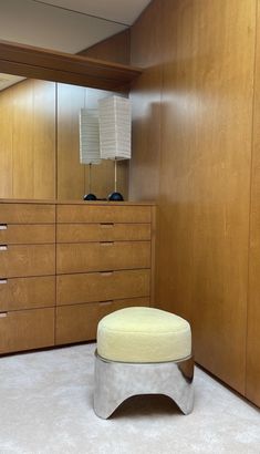 an ottoman sits in the middle of a room with wooden cabinets and dressers behind it