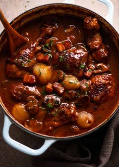 a pot filled with meat and potatoes on top of a table next to a wooden spoon