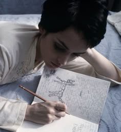 a woman laying on top of a bed holding a pen and paper