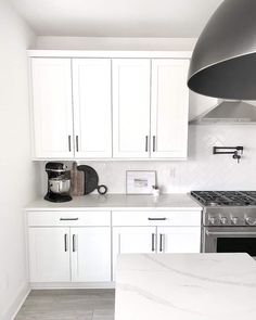 a kitchen with white cabinets and marble counter tops, an oven hood over the stove