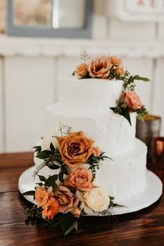 a three tiered white cake with orange flowers on the side and greenery around it