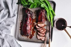 some meat and greens on a tray with spoons next to it, including broccoli