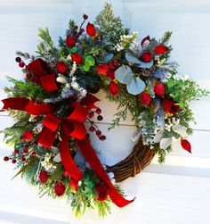 a wreath with red ribbon and greenery on the front door, decorated with holly