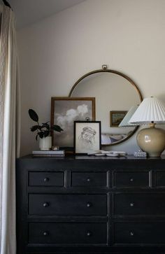 a dresser with a mirror, lamp and pictures on it