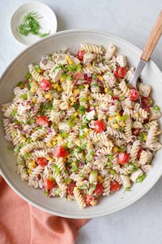 a white bowl filled with pasta salad next to a wooden spoon