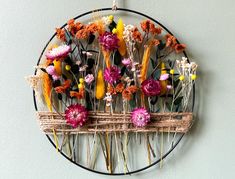 an arrangement of flowers arranged on a circular wire frame hanging on the wall in front of a white wall