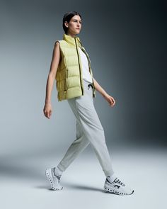 a woman is walking while wearing a yellow vest and white pants with sneakers on her feet