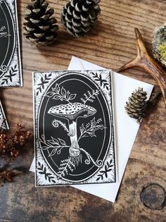 three cards with black and white designs on them next to pine cones, antlers and other decorations