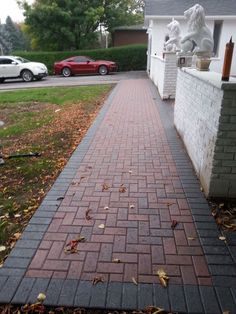 a brick walkway in front of a house with cars parked on the street behind it