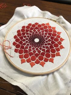 a red and white circular design is on a piece of cloth next to some thread