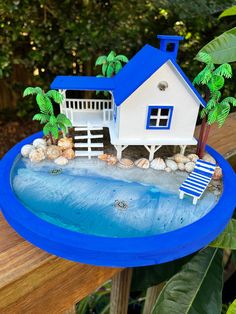 a blue and white house sitting on top of a wooden table next to a body of water