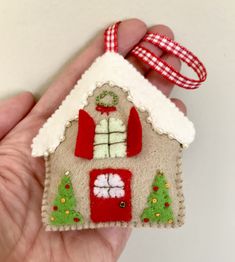 a hand holding a small felt ornament with a house on it's side