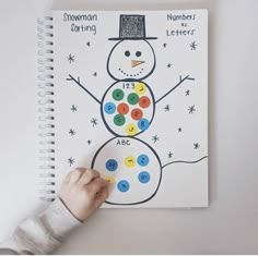 a child's hand is drawing a snowman on a white notebook with numbers and letters