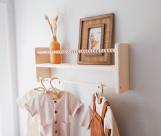 two baby clothes are hanging on the wall next to a shelf with an orange vase