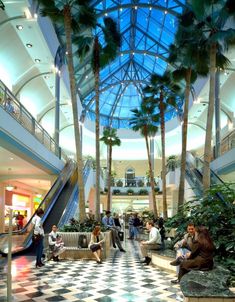 people are sitting and walking in the lobby of a shopping mall with palm trees on either side