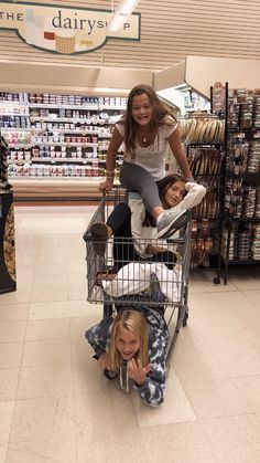 two women pushing a shopping cart in a grocery store while another woman sits on the floor